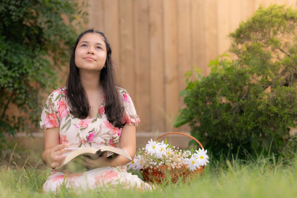 A peaceful outdoor reading scene with a floral dress against a wooden fence and garden backdrop. In Pearland, TX
