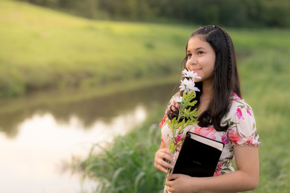 A woman in a floral dress sits peacefully outdoors while holding a wildflower and enjoying nature on a sunny day. In Pearland, TX