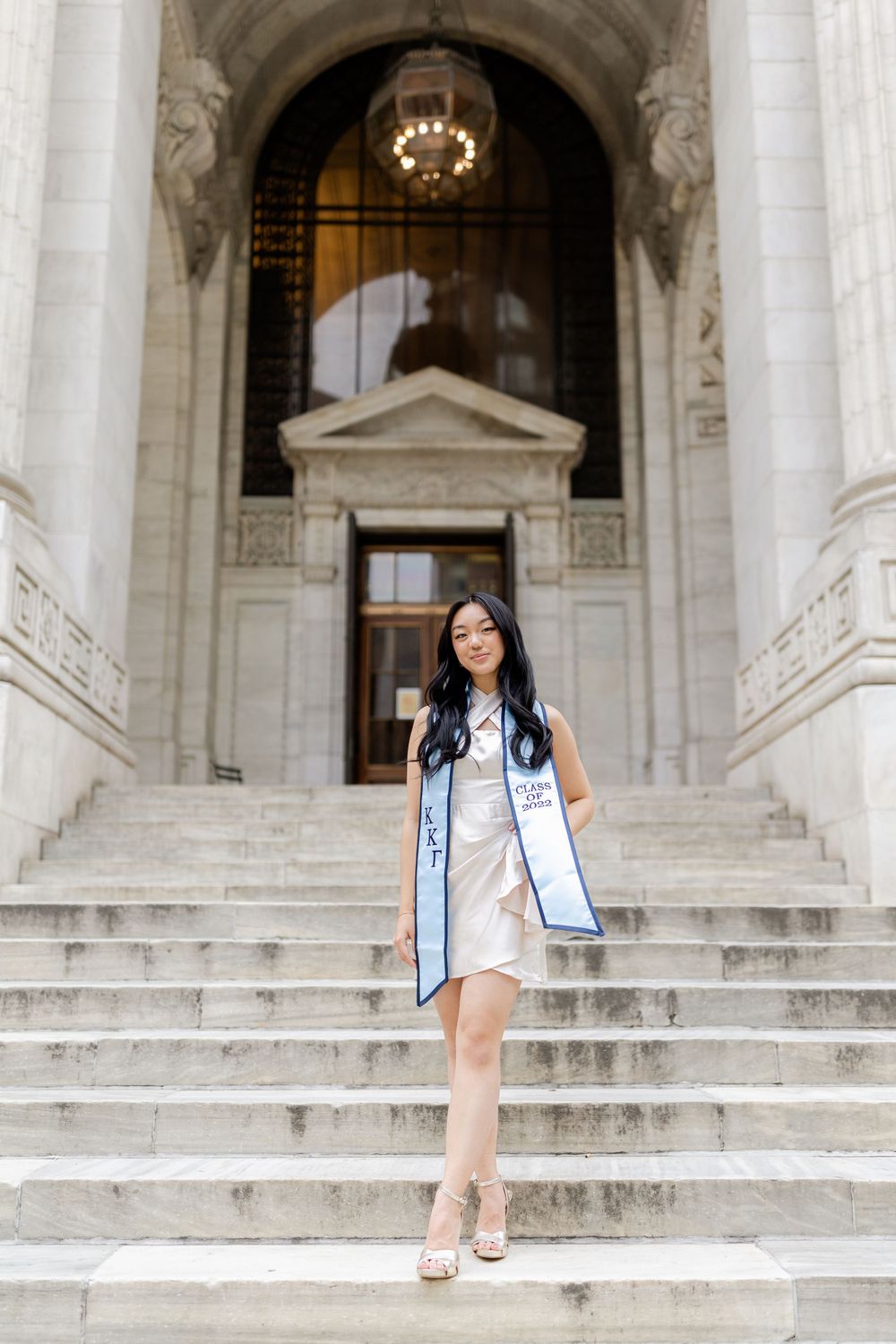 Graduate in light blue stole poses on grand marble staircase.
