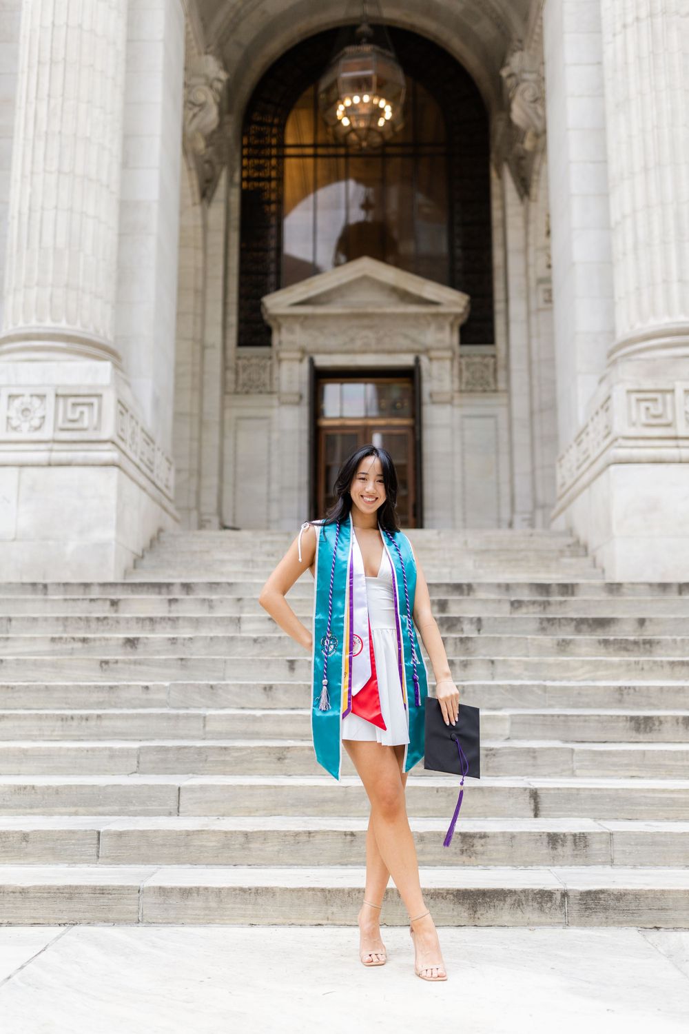 Graduate in teal stole stands elegantly on ornate stone steps.