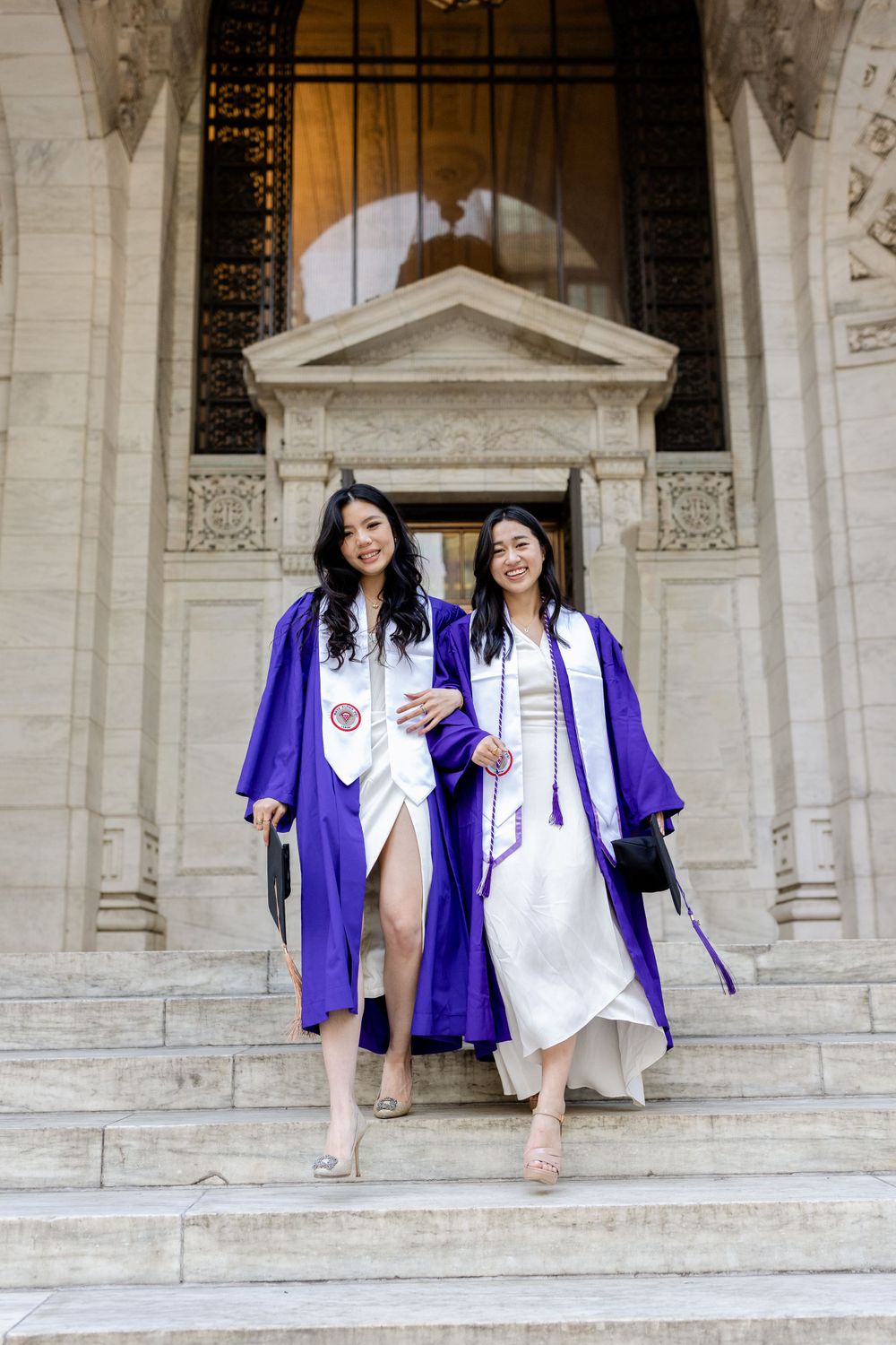 Two graduates descend grand stone steps in purple graduation robes.
