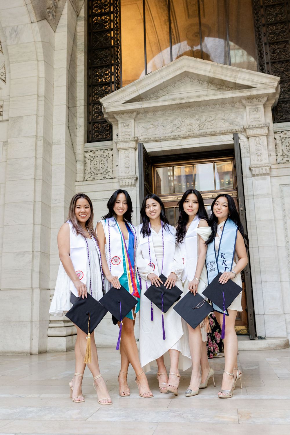 Graduates pose with their caps on a grand marble staircase entrance during commencement day.