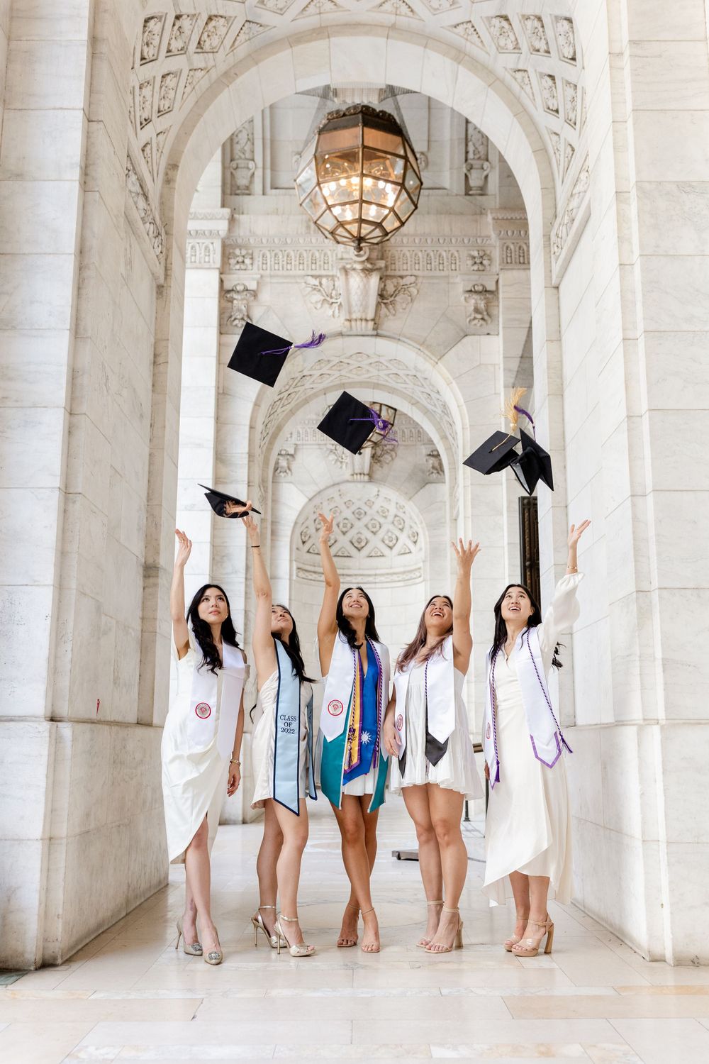 Graduates throw their caps under ornate archways with hanging vintage lanterns.