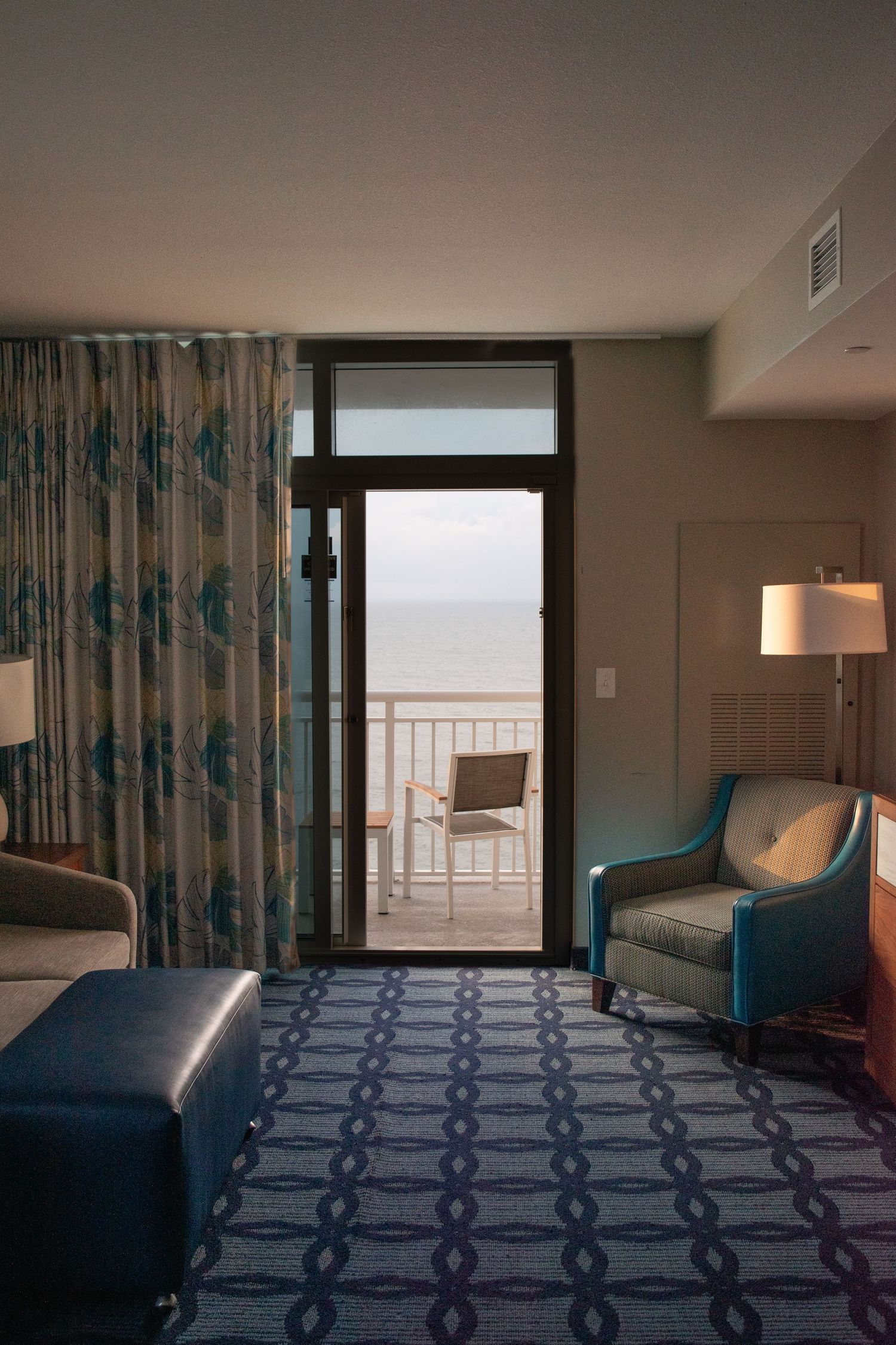 The interior of a hotel room, light streaming in from the balcony overlooking an oceanfront view