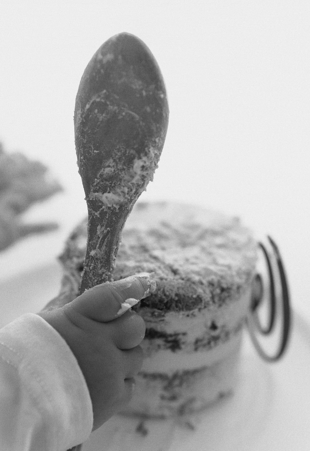 A close-up black and white photo of a hand holding a spoon with cake crumbs and frosting.