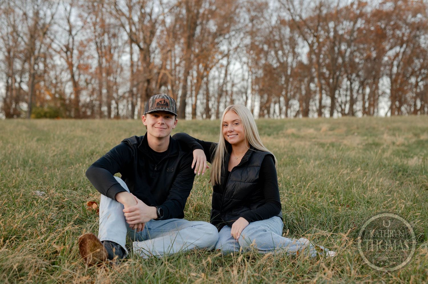 sibling poses casually on grassy hillside during fall photoshoot.