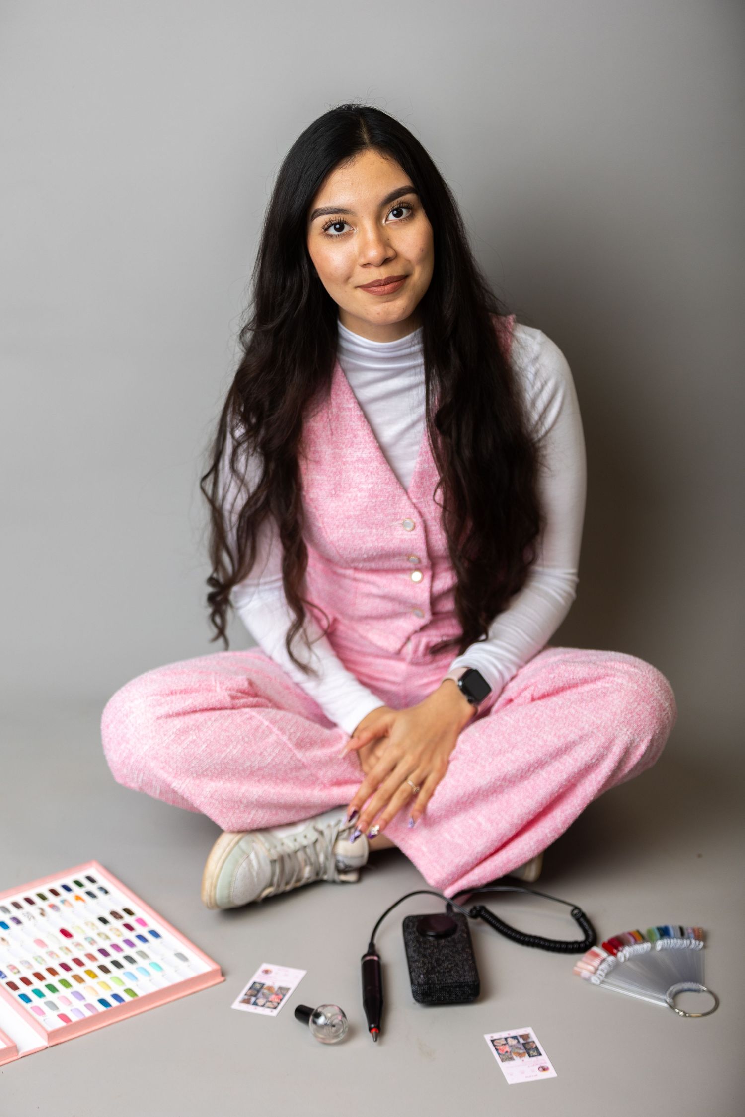 A person in pink loungewear sits cross-legged on the floor with business supplies and cards.