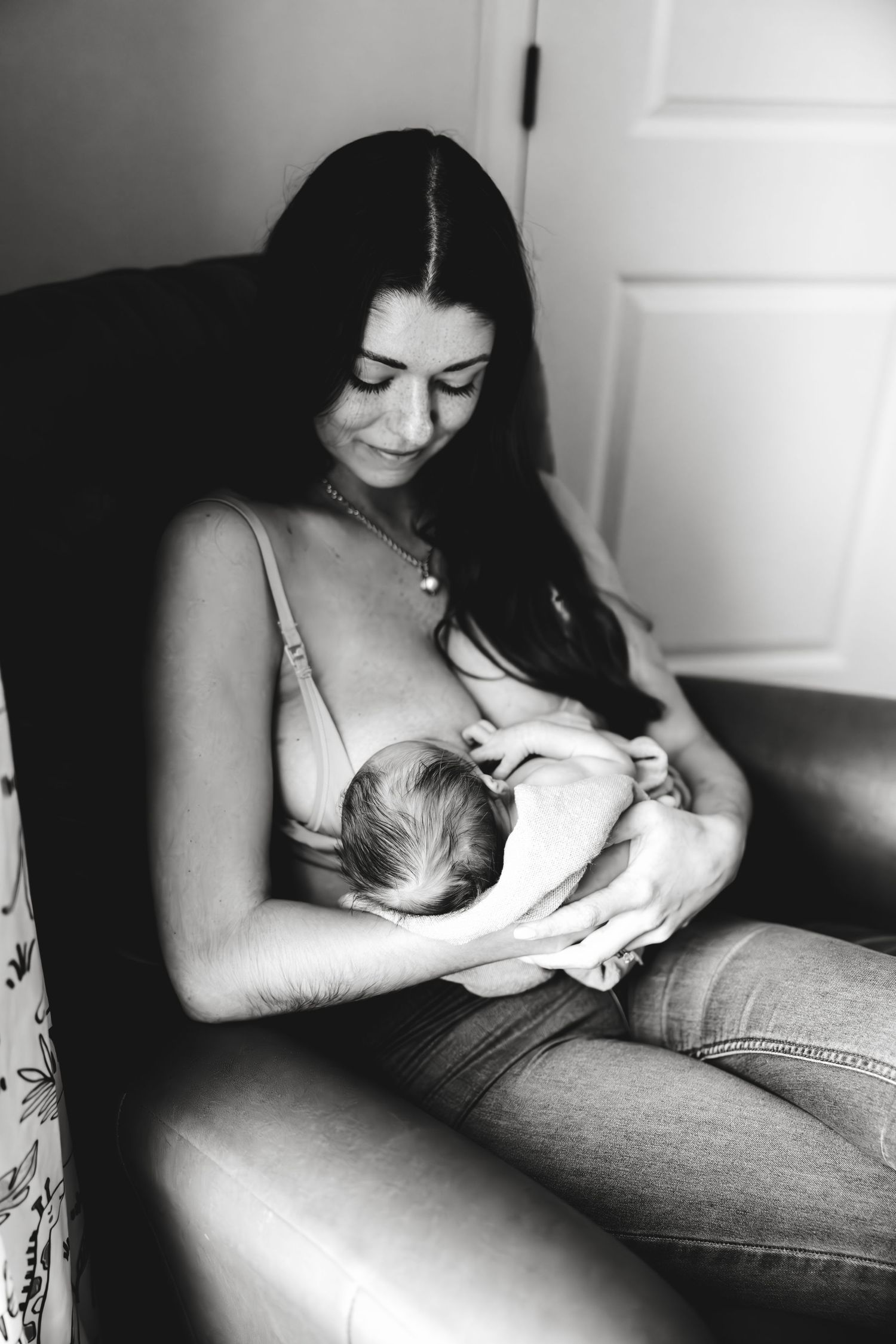 Intimate black and white photograph capturing tender moment of breastfeeding between mother and newborn baby.