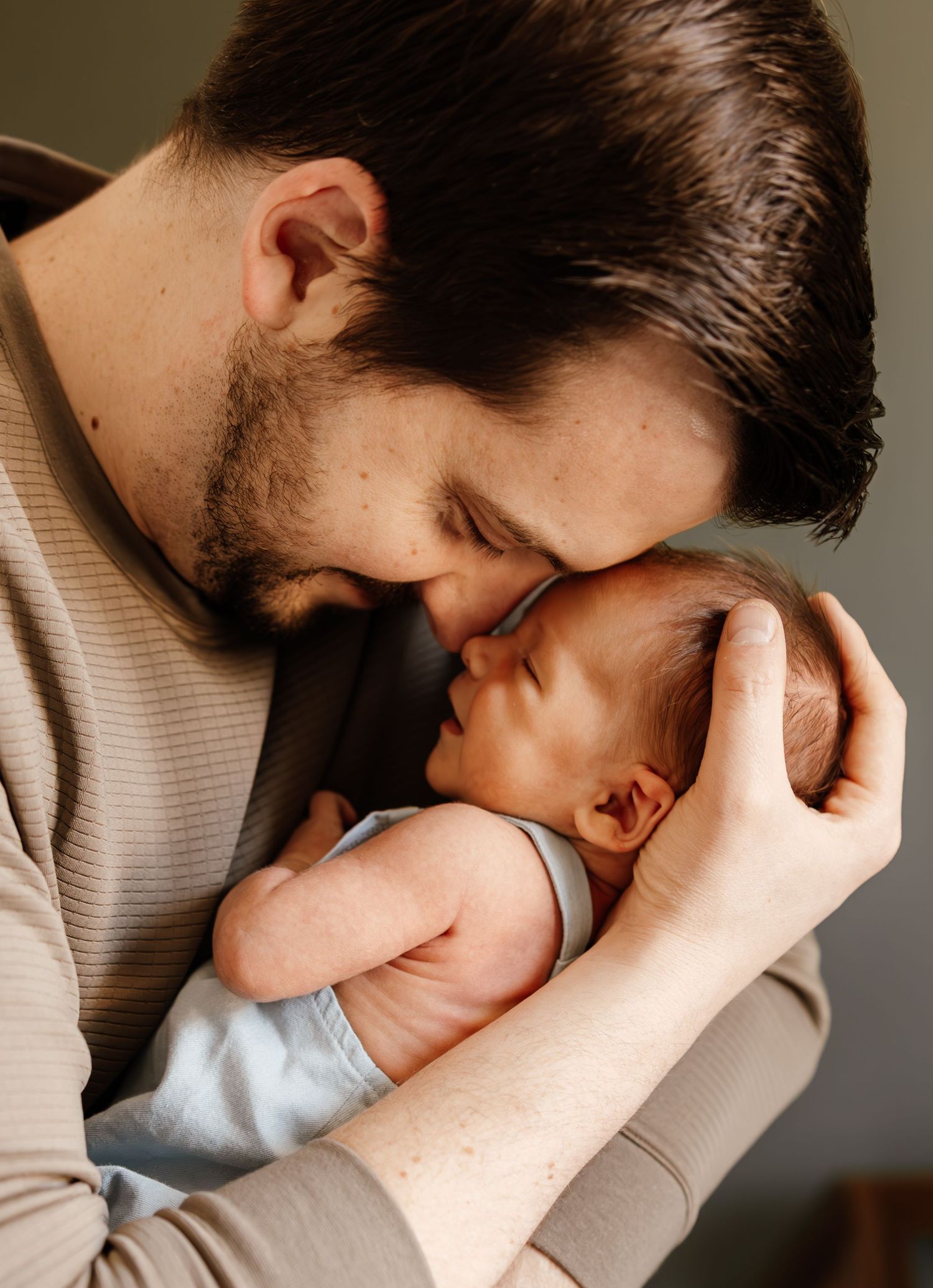 A tender moment between parent and sleeping newborn baby captured in warm, intimate lighting.