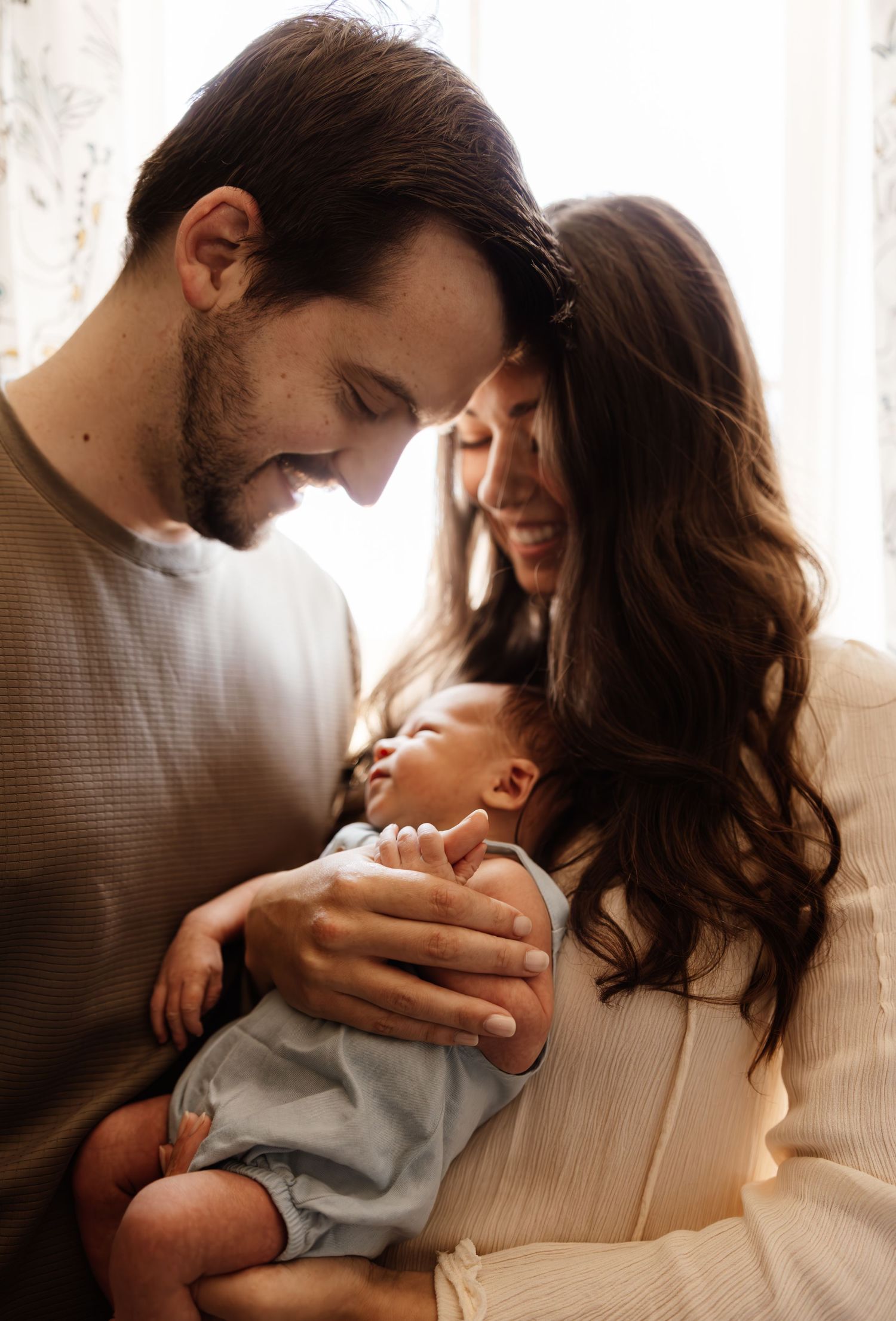 A loving couple shares a tender moment with their newborn baby in a warm, intimate indoor setting.
