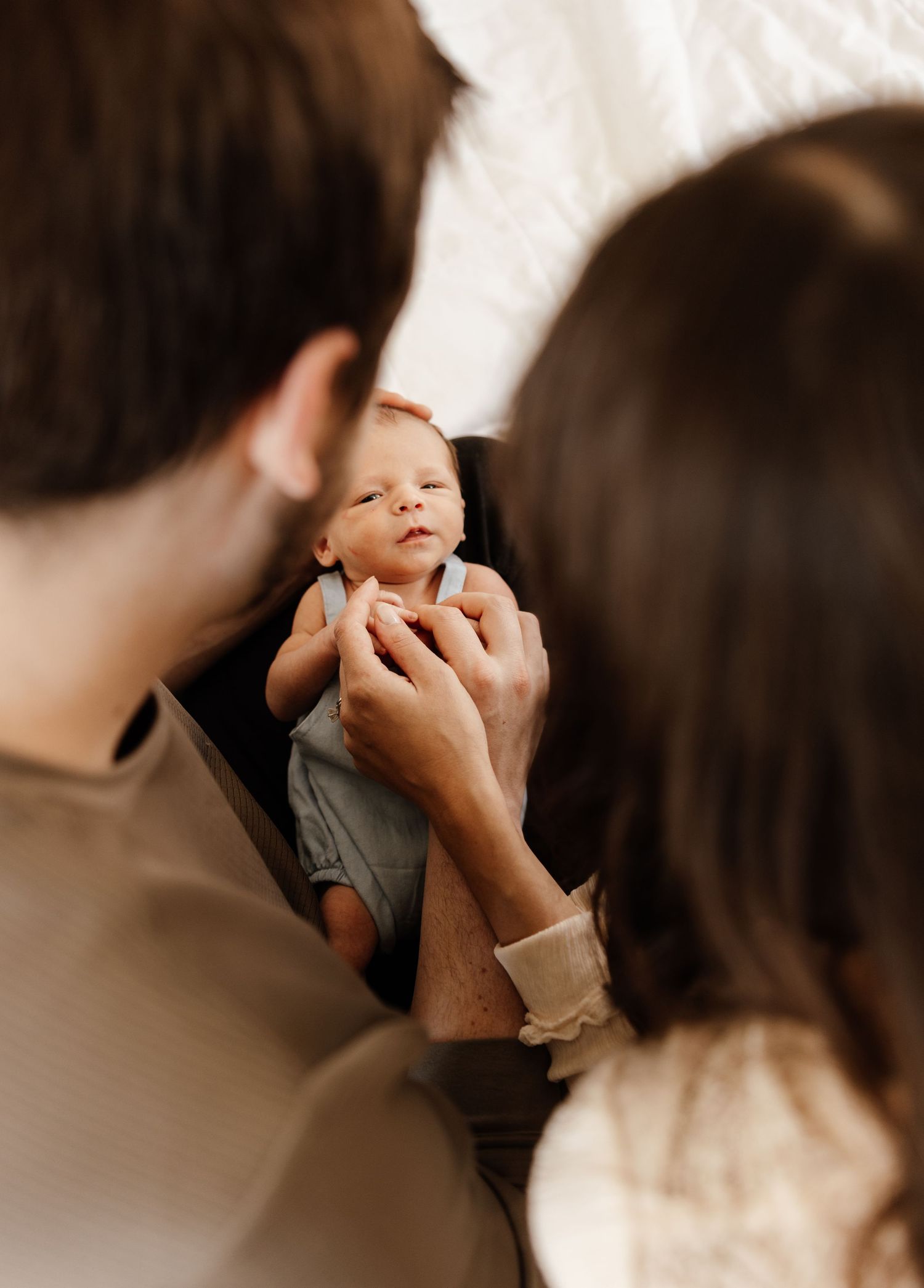 Parents tenderly hold their sleeping newborn baby in gray clothes while sharing an intimate family moment together.