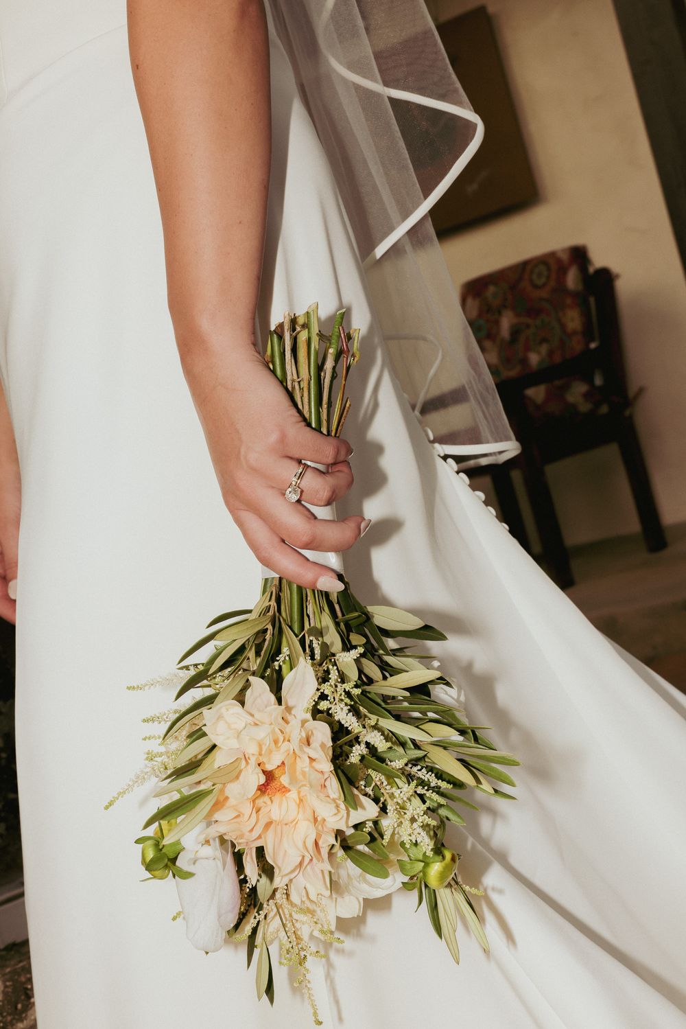 Close-up of a bridal bouquet with white flowers and greenery against a flowing white wedding dress.