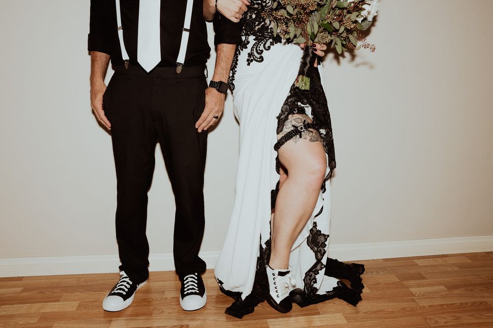 Cropped view of couple's legs showing groom in black pants and bride in white dress with black details.