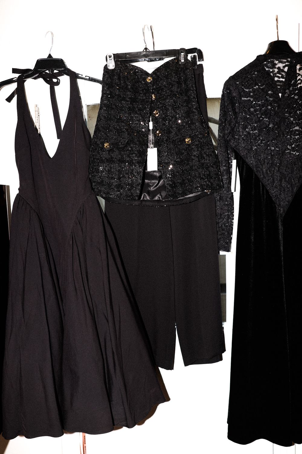 Collection of black formal dresses including lace and halter styles hanging on clothing rack.