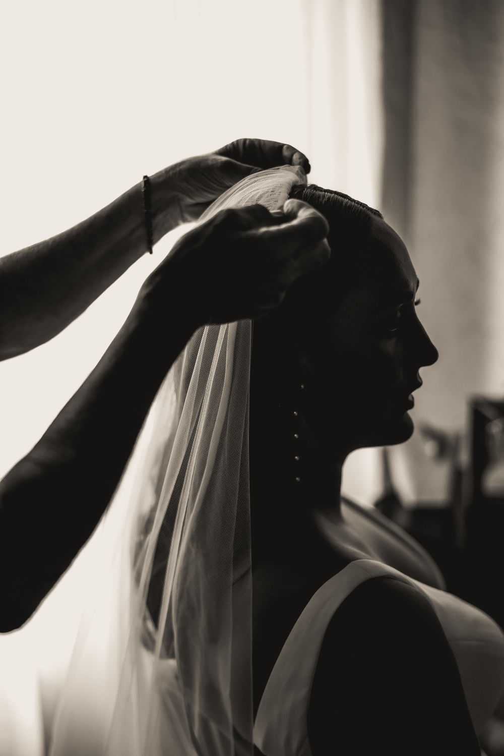 Silhouette of a bride getting her veil adjusted in dramatic black and white photography.