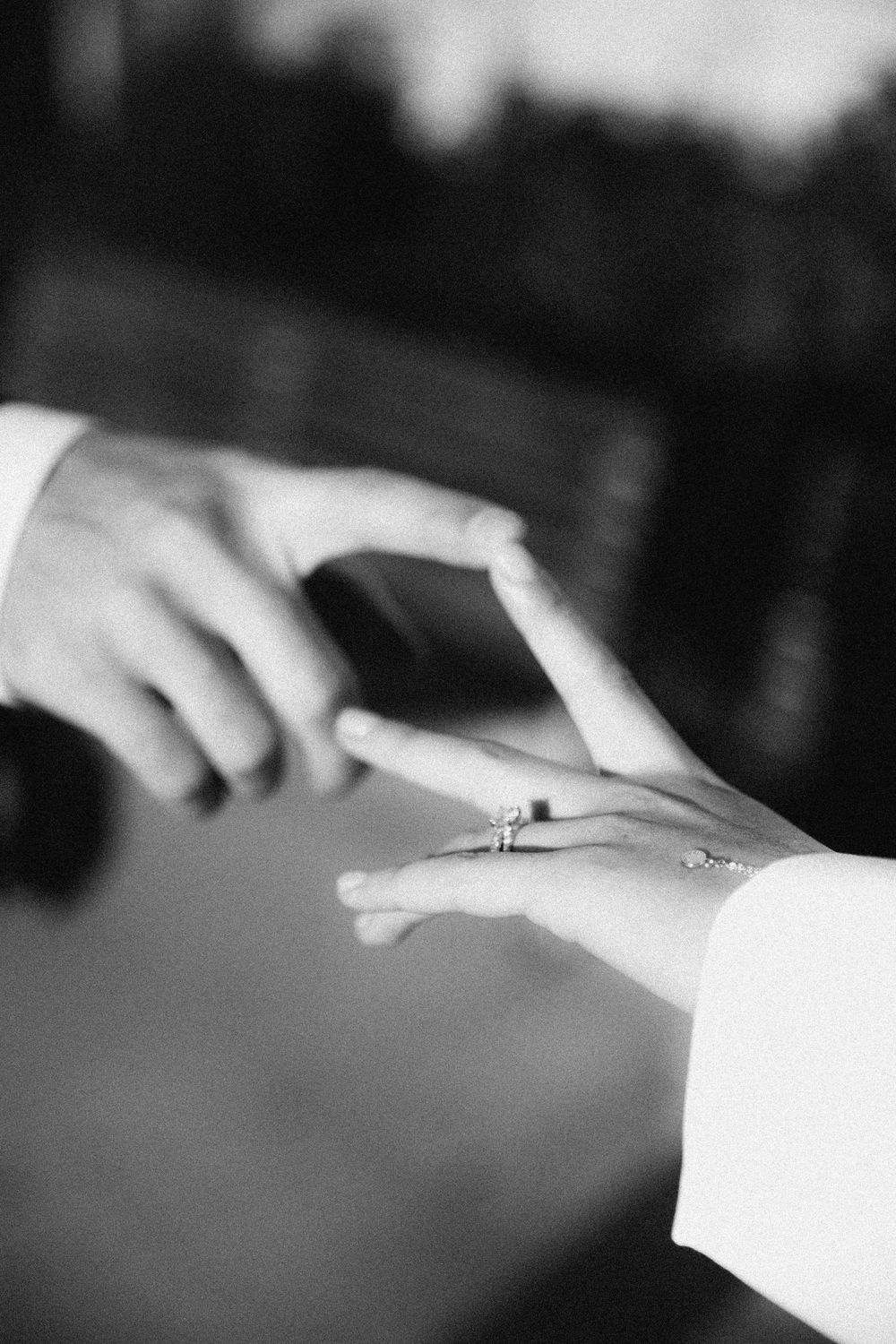 Close-up black and white photo showing a hand placing an engagement ring on another person's finger.