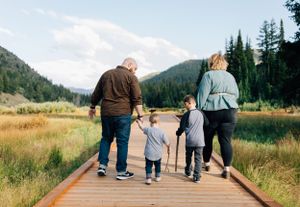 Family walking together on a wooden boardwalk trail surrounded by mountains and evergreen forest.