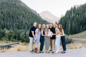 A group poses together on a mountain path with evergreen forest and peaks in the background.