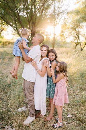 Warm sunset family portrait with children embracing in golden field.