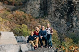 Group sitting together on rocky mountain ledge with dramatic cliff face backdrop.