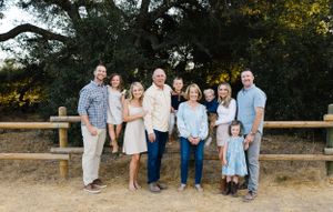 A group gathers in front of a rustic wooden fence and large tree for an outdoor photo.