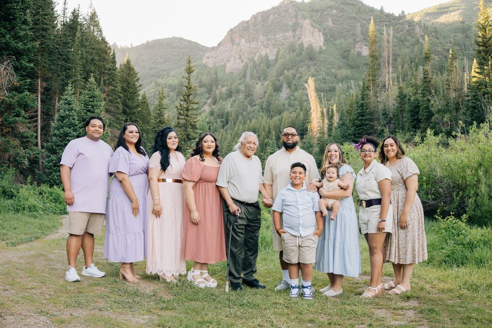 A large group poses together in pastel dresses against a mountain backdrop with evergreen trees.