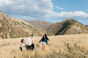 A small group walks through tall grass with mountains in the background.