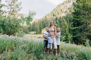 Outdoor portrait in alpine meadow with mountain peaks and evergreen forest in background.