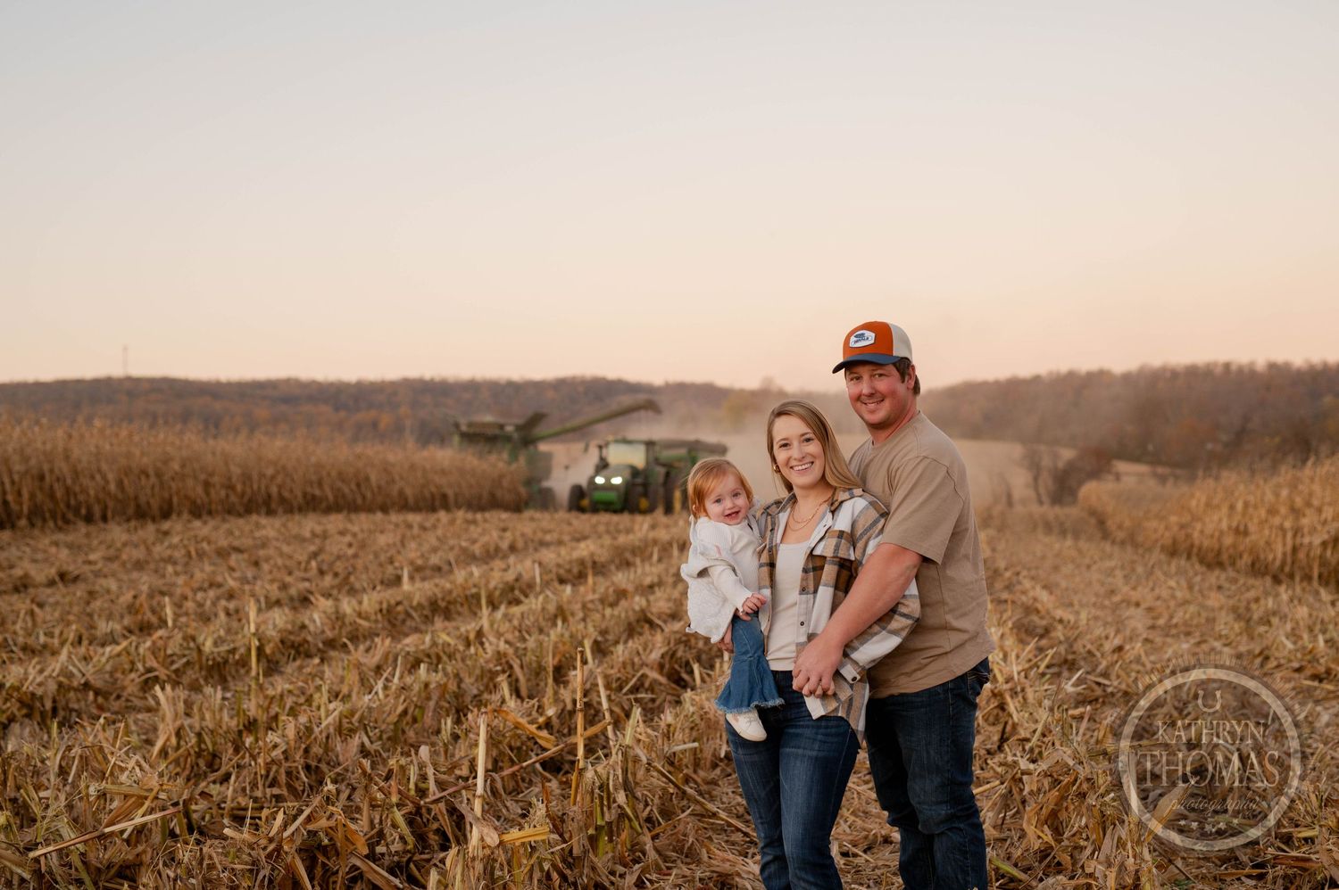 Family standing together in harvested cornfield with farm equipment visible.