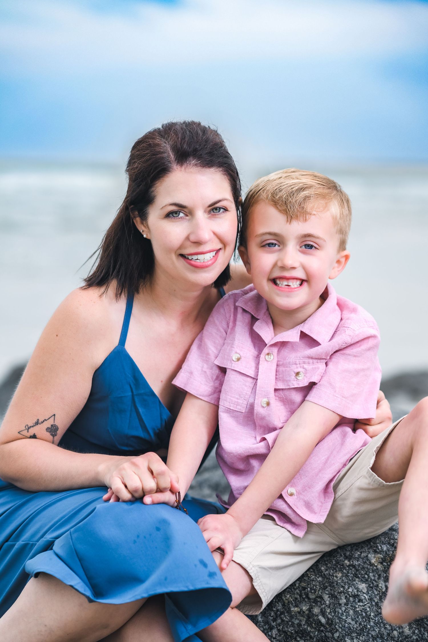 A mother and young child sitting together outdoors on a sunny day at the beach.