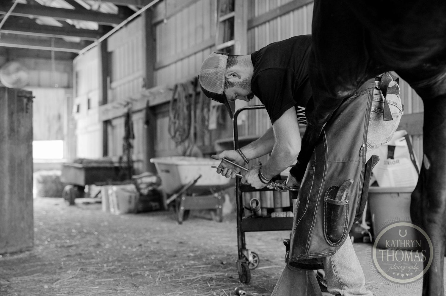 Black and white photograph of farrier equipment being used in stable setting.