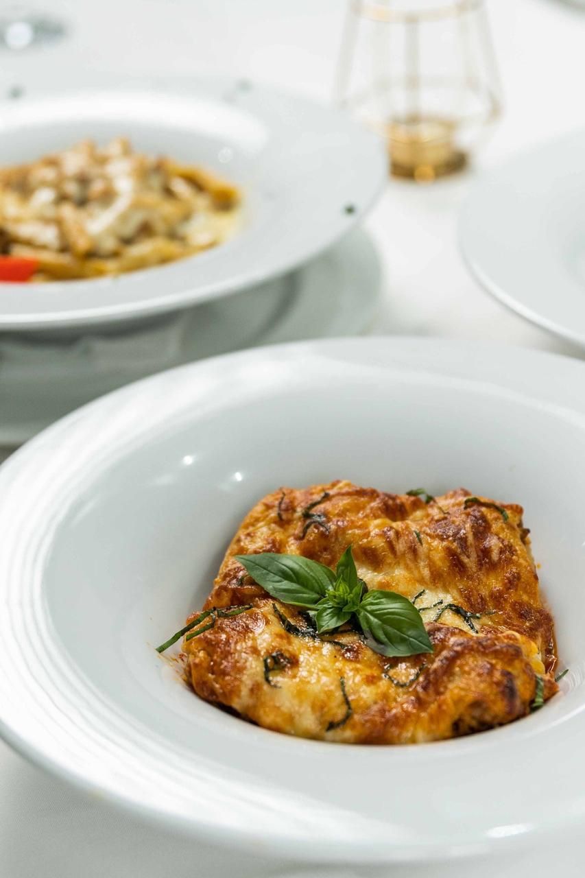 Baked pasta dish garnished with fresh basil in white restaurant plate.
