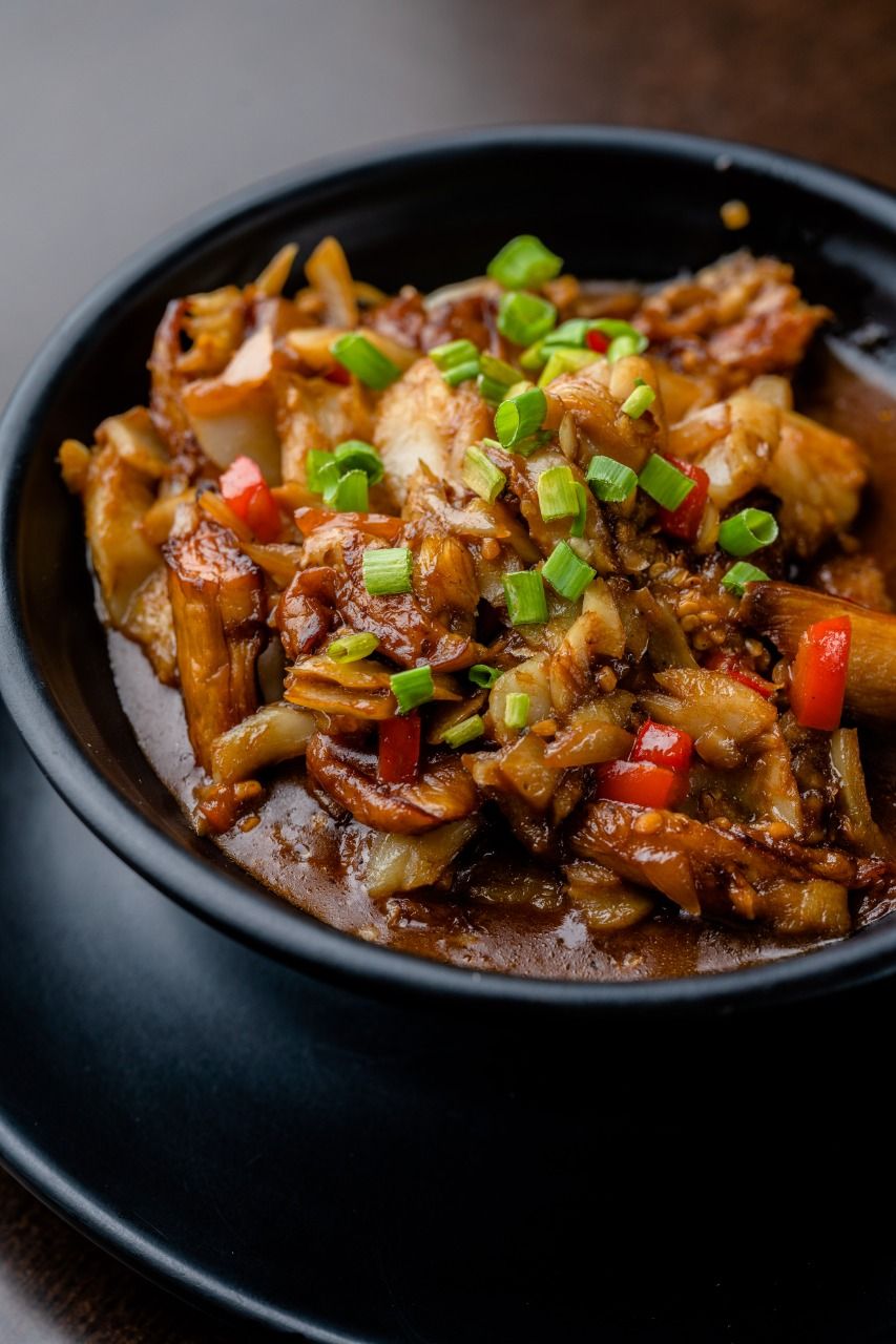 Stir-fried Asian dish with vegetables and meat garnished with green onions in black bowl.