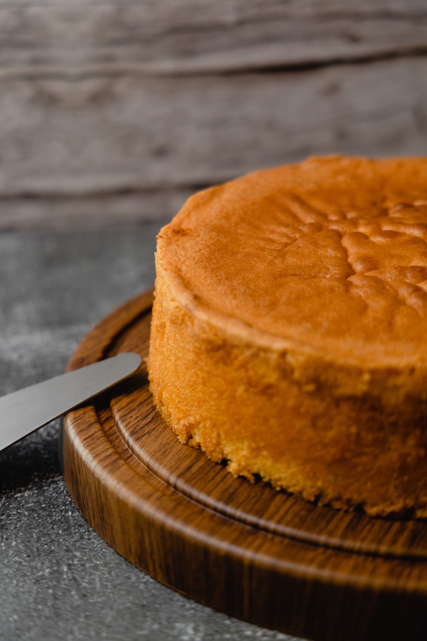 Golden brown sponge cake on wooden cutting board with knife.