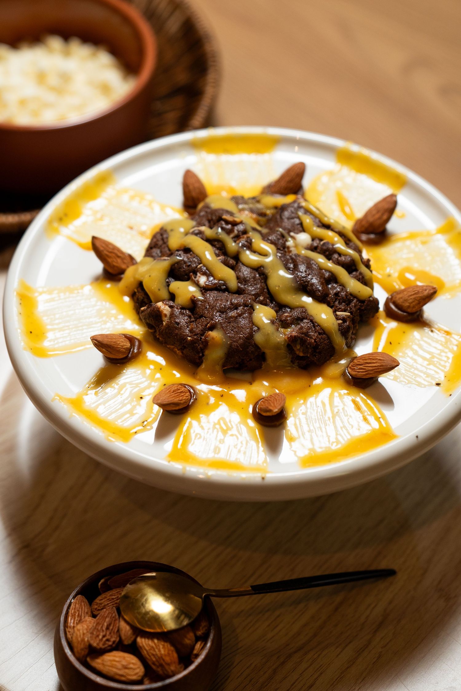 A creamy white dessert bowl topped with orange slices, chocolate drizzle, and scattered almonds on a wooden surface.