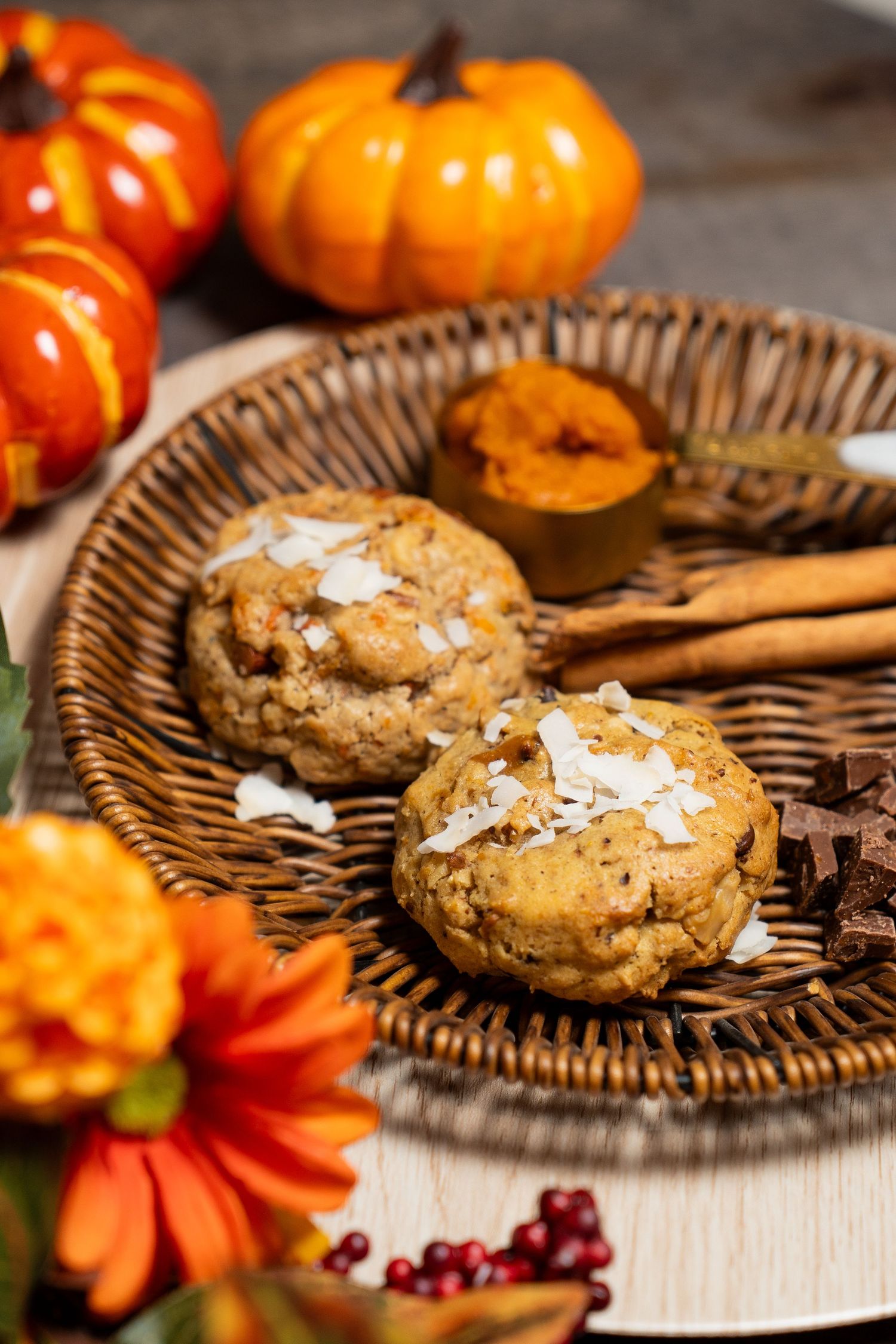 Homemade chocolate chip cookies topped with sea salt flakes on a woven plate with mini pumpkins and fall decor.