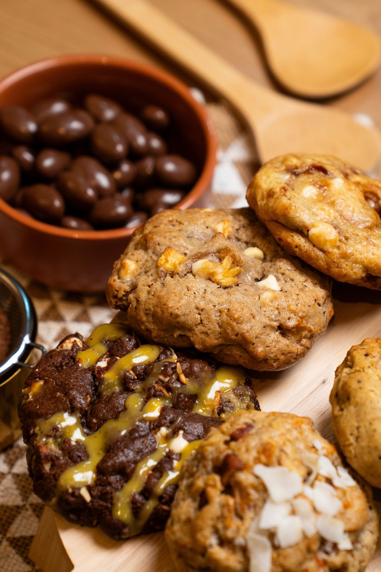 Close-up view of chocolate chip cookies with nuts and dark chocolate drizzle arranged on a wooden surface.