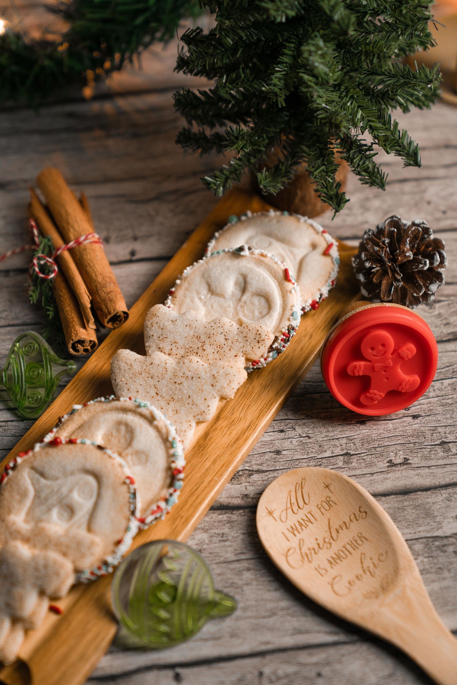 Holiday cookies and festive decorations arranged on a wooden board with cinnamon sticks and pine branches.