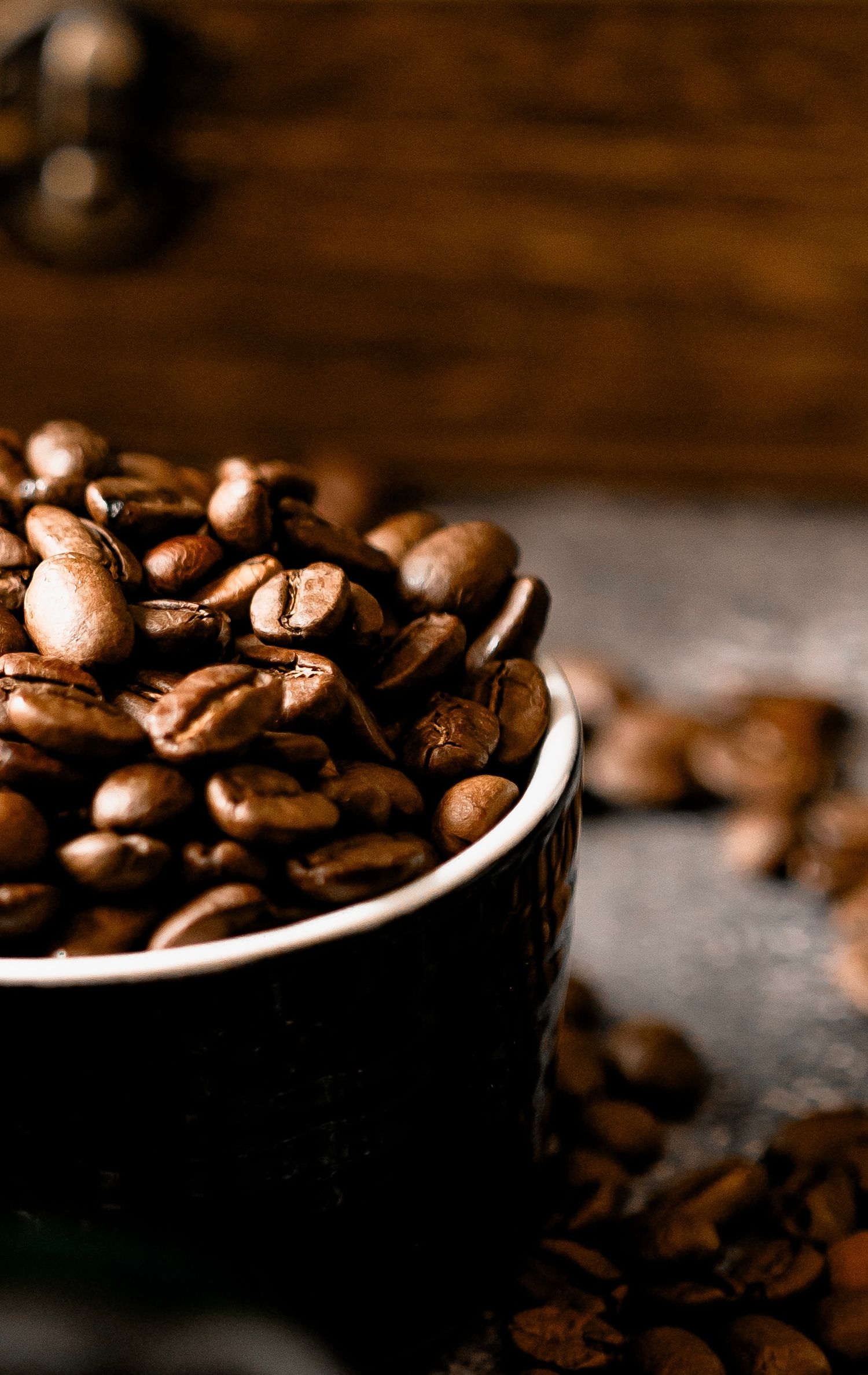 Close-up of roasted coffee beans spilling from dark cup on wooden surface.