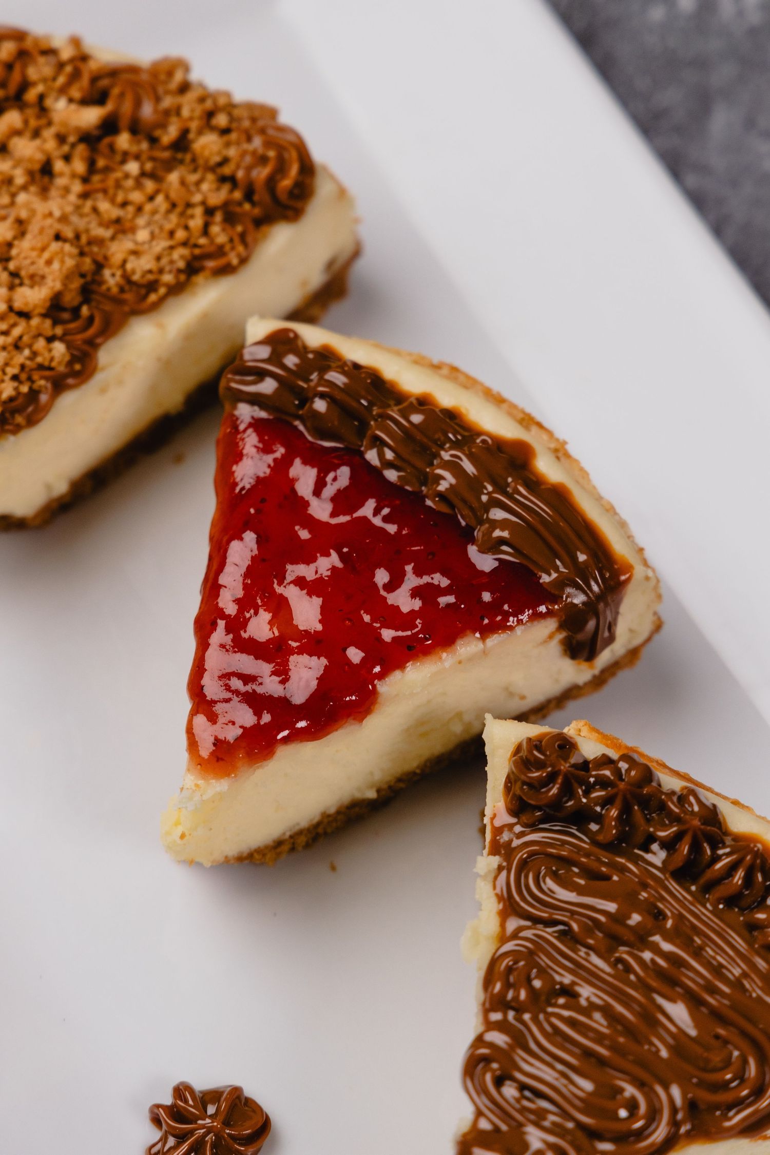 Three slices of cheesecake with different toppings on white plate.