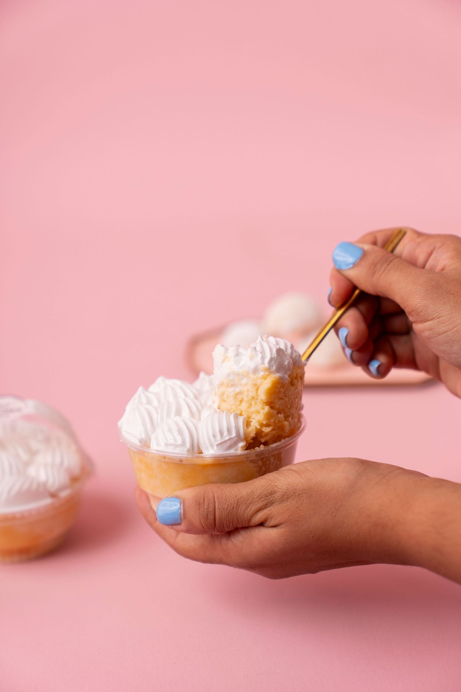 Hand with blue nail polish holds a cream-filled pastry against a pink background in a sequence of progressive bites.