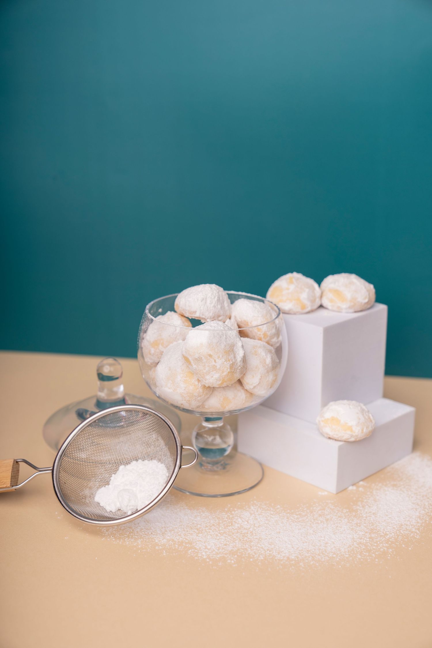 White powdered snowball cookies displayed in glass bowl and white boxes against teal background.