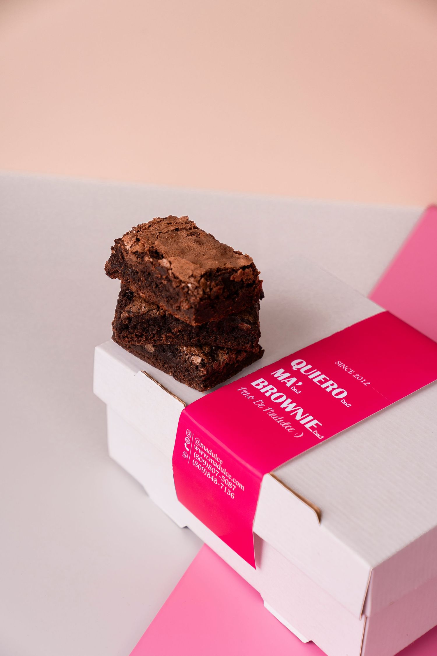 Chocolate brownies stacked on white box with pink branding label.