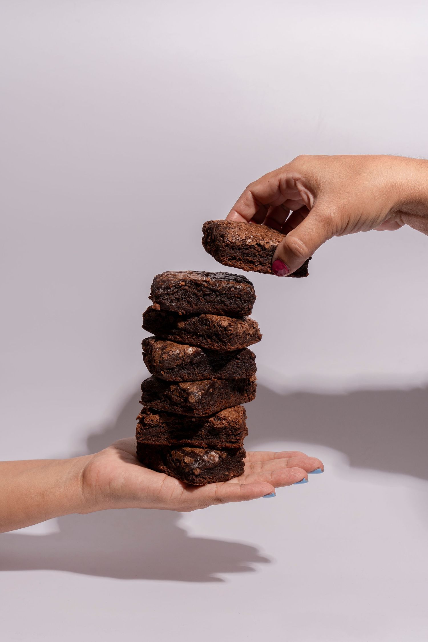 Stack of chocolate brownies being held between two hands against a white background.