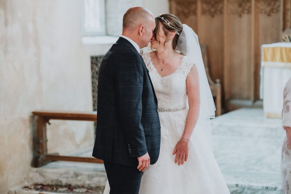 A romantic wedding moment captured in a rustic stone church interior with soft natural lighting.