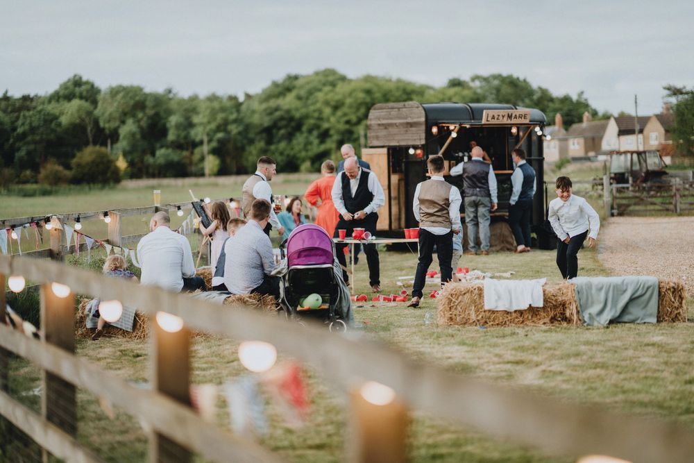 Outdoor gathering in a field with guests, musical instruments, and string lights setup for an event.