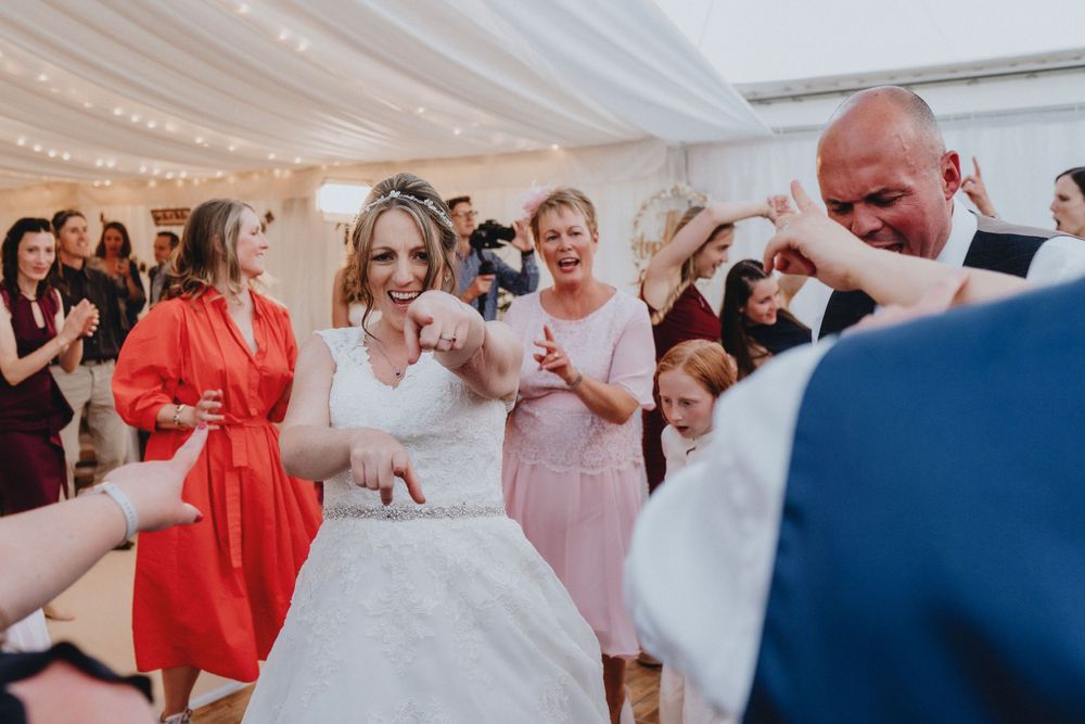 Wedding guests celebrate on the dance floor as a bride in white dress dances surrounded by loved ones.