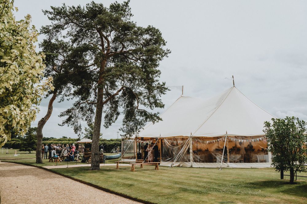 A large white wedding tent at Lattenbury Hill set up on a manicured lawn with tall pine trees and guests gathering outside.