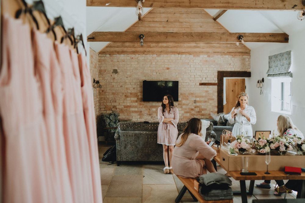 Wedding party getting ready in rustic barn venue with exposed wooden beams and blush pink decor details.