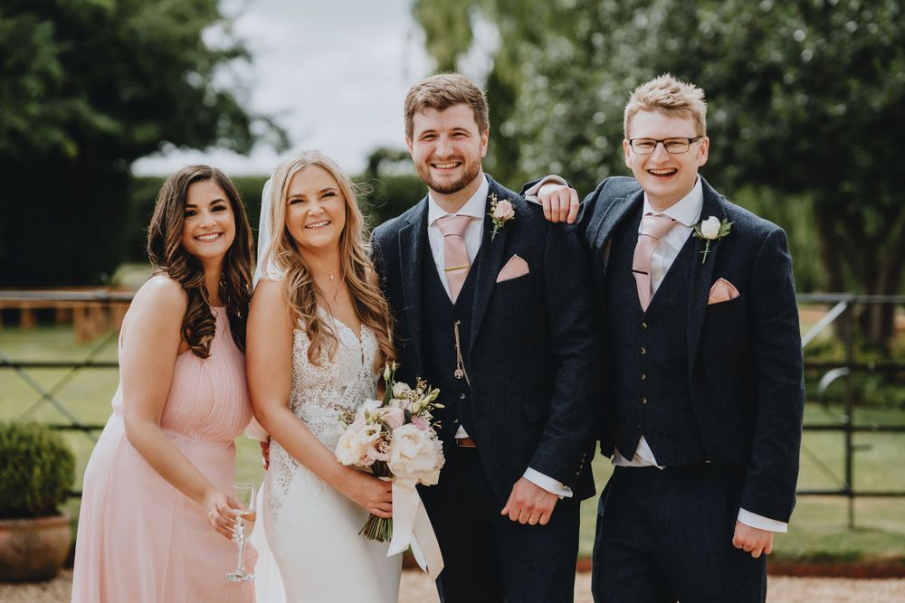 Wedding party members in formal attire pose together outdoors during a spring celebration.